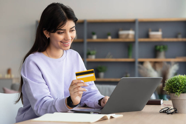 Femme souriante utilisant ordinateur portable et carte de crédit à la maison - Photo, image
