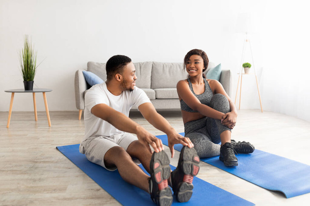 Атлетическая чёрная пара делает упражнения на спортивных ковриках дома, полной длины. Здоровый образ жизни - Фото, изображение