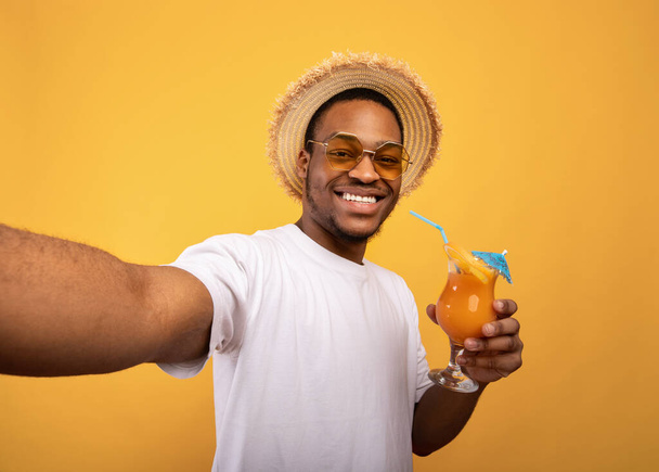 Hyvännäköinen musta kaveri kesällä kulumista juominen namia hedelmiä cocktail ja ottaen selfie keltainen studio tausta - Valokuva, kuva