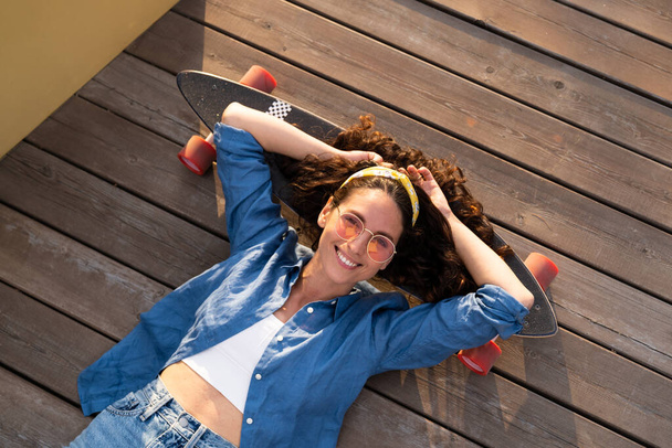 Carefree smiling woman on skateboard relaxed and happy. Trendy girl skateboarder lying on longboard - Photo, Image
