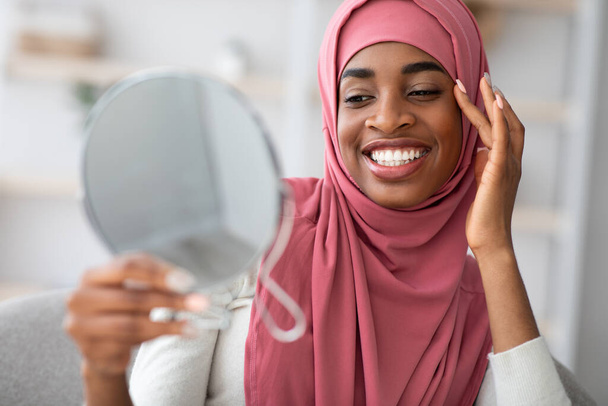 Koncepcja piękna. Atrakcyjny czarny islamski lady w hidżab patrząc w lustro powiększające - Zdjęcie, obraz
