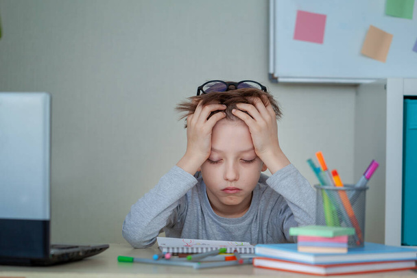 Unhappy and strssed school boy studying with a notebooks on his desk at home. Child is tired of online learning. Education and childhood concept - Foto, imagen