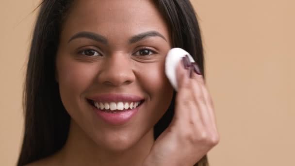 Afrikai nő használ Cotton Pad alkalmazása arc por, bézs háttér - Felvétel, videó