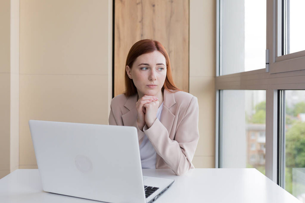 Upset red-haired business woman working at computer sitting in the office, has severe stress and headache - Фото, зображення
