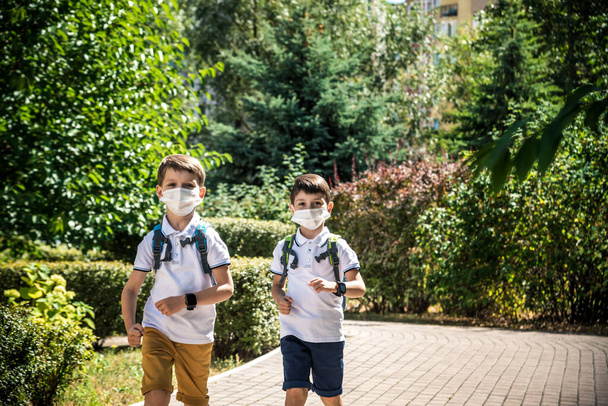 Счастливые школьники в масках бегут от радости возвращения в школу во время карантина Ковид-19. - Фото, изображение