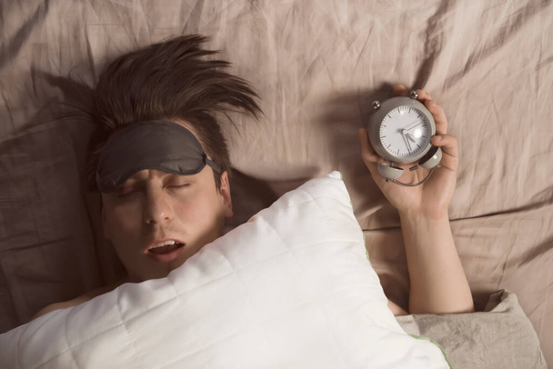 Egy fiatal férfi kezei a takaró alól egy ébresztőórát tartanak szürkében..  - Fotó, kép