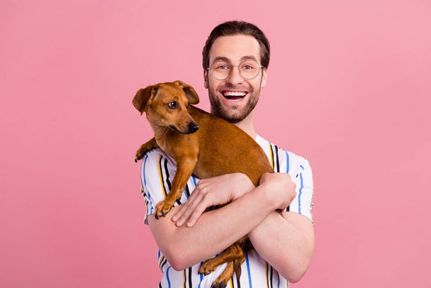 Foto Porträt Mann in T-Shirt Brille lachen halten kleinen Hund isoliert pastellrosa Hintergrund - Foto, Bild