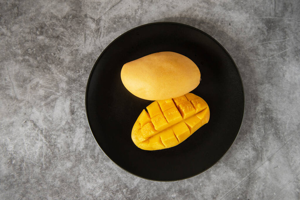 Fresh yellow mango fruit in a black plate - Fotó, kép