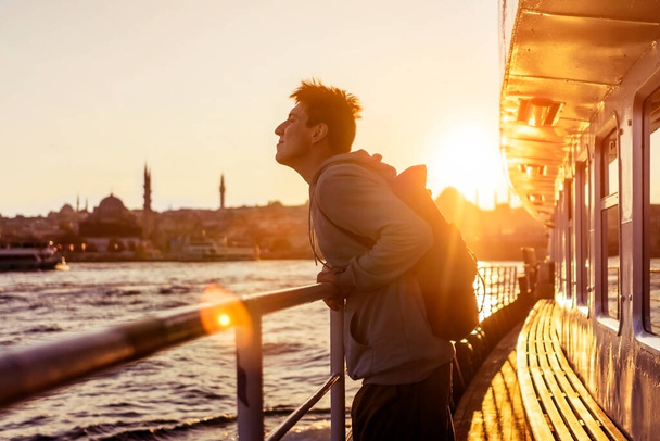 フェリーに乗った若い笑顔の男がトルコのイスタンブールの海岸に浮かぶ. - 写真・画像