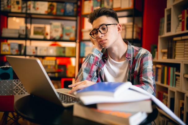 Um jovem caucasiano, estudante sentado à mesa com laptop em casa ou biblioteca de fundo. - Foto, Imagem