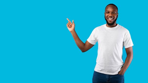 Fekete ember mutató ujját félre mosolygó kamera, kék háttér - Fotó, kép