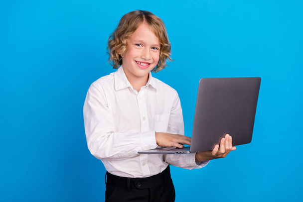 Portrait of attractive cheerful boy using laptop typing web lesson isolated over bright blue color background - Fotografie, Obrázek