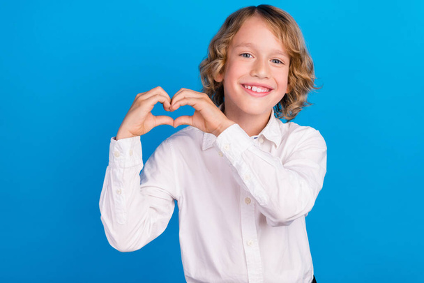 Portrait of attractive cheerful boy showing heart symbol amour cupid isolated over bright blue color background - Foto, immagini