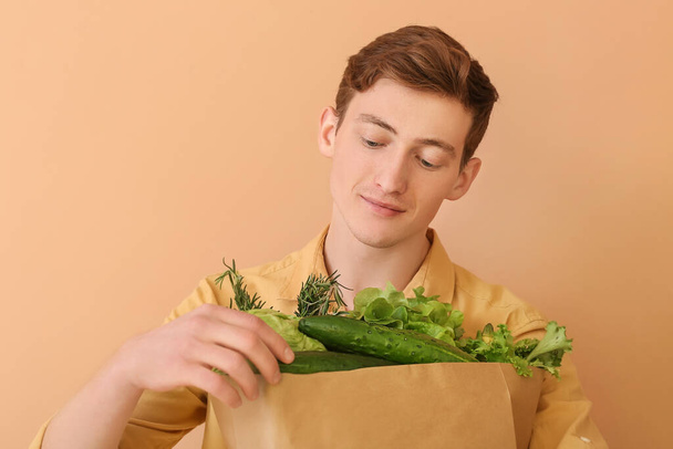 Young man holding paper bag with fresh vegetables on color background - Photo, image