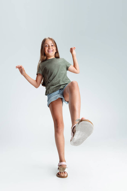 Full-length portrait of beautiful preschool smiling girl stepping in air isolated on gray studio background. Childhood, education, emotion concept - Fotoğraf, Görsel