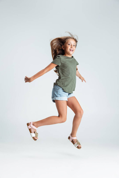 Pełnowymiarowy portret pięknej przedszkolanki uśmiechniętej dziewczyny skaczącej, grającej w izolacji na szarym tle studia. Miejsce na reklamę. Dzieciństwo, edukacja, koncepcja emocji - Zdjęcie, obraz