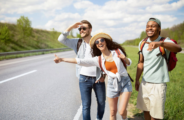 Различные друзья стоят на обочине дороги, останавливают машины, путешествуют автостопом бесплатно, наслаждаются летними каникулами - Фото, изображение