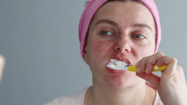 Giovane femmina con una benda in testa si pulisce i denti con uno spazzolino di plastica in bagno. Mattina assistenza sanitaria - Filmati, video