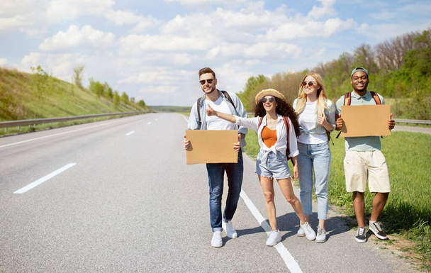 Group of multiethnic friends with empty signs hitchhiking on road, catching ride, traveling by autostop, copy space - Photo, Image