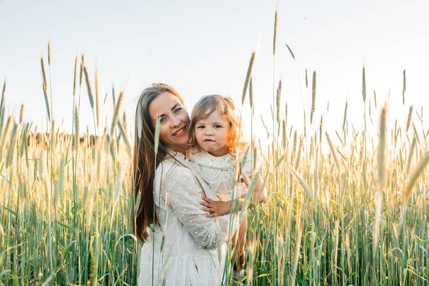 Happy family, mother in a dress with a cute little baby on a golden wheat field at sunset. summer day - Foto, Imagem