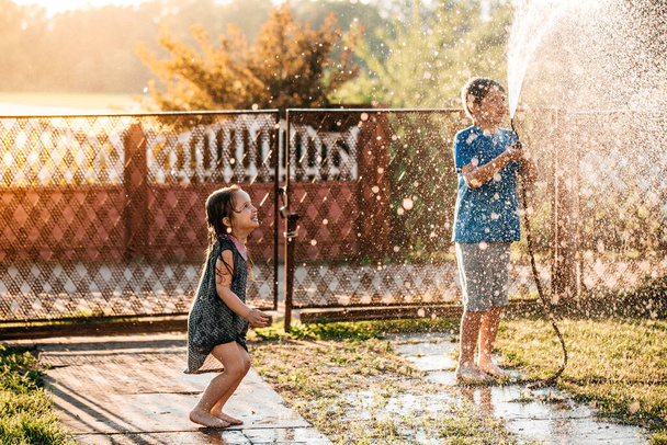 little children playing together with a garden hose on hot and sunny summer day on sunset - Foto, immagini
