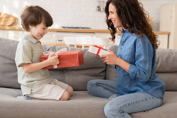 Mom and son celebrate birthday together: happy mum and excited son sit on couch hold gifts smiling - Photo, Image