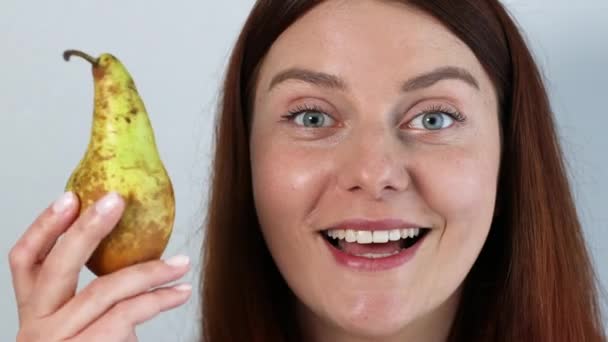 Smiling pensive young woman holding fresh ripe yellow pear in hand and smells organic fruit isolated on gray background. - Footage, Video