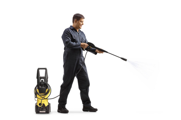 Full length profile shot of a worker in a uniform cleaning with a pressure washer machine isolated on white background - Foto, afbeelding
