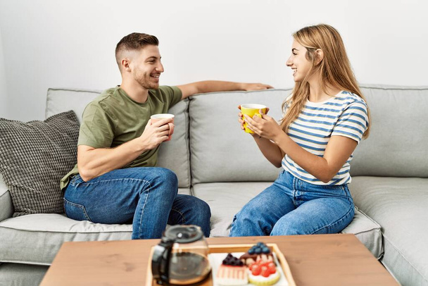 Young hispanic couple smiling happy having breakfast sitting on the sofa at home. - Foto, Imagem