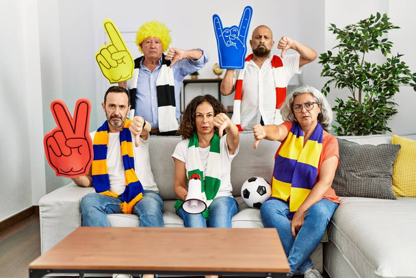 Grupo de personas mayores que apoyan al equipo de fútbol en casa con la cara enojada, signo negativo que muestra aversión con los pulgares hacia abajo, concepto de rechazo  - Foto, Imagen