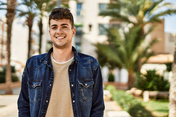 Jonge Spaanse man glimlachend blij staand in de stad - Foto, afbeelding