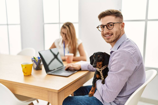 Δύο επαγγελματίες χαμογελάνε ευτυχισμένοι δουλεύοντας με το σκύλο στο γραφείο. - Φωτογραφία, εικόνα