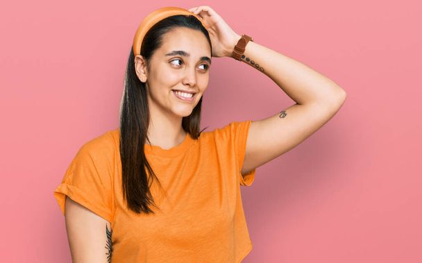 Mujer hispana joven vistiendo ropa casual sonriendo confiada tocando el cabello con gesto de la mano hacia arriba, posando atractivo y de moda  - Foto, Imagen