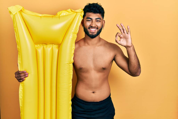 Arab férfi szakállas fürdőruha és a kezében nyári matrac úszó csinál rendben jel ujjakkal, mosolygós barátságos gesztus kiváló szimbólum  - Fotó, kép