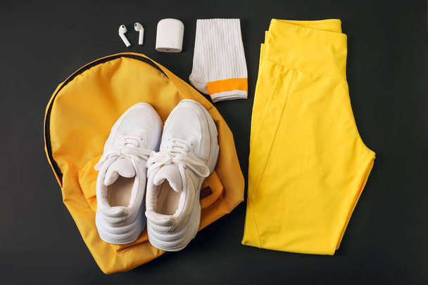 Sportschoenen, joggingbroek, rugzak, sokken en oortelefoons op donkere achtergrond - Foto, afbeelding