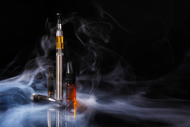Cigarrillo electrónico con aceite sobre fondo oscuro con humo - Foto, imagen