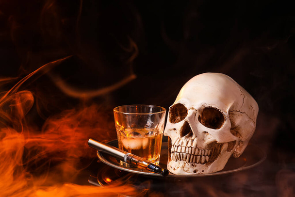 Tray with electronic cigarette, glass of whisky and human skull on dark background with fume - Photo, Image