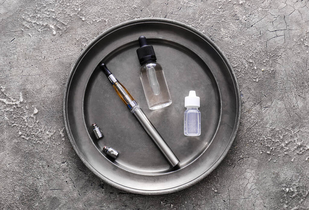 Tray with electronic cigarette and oil on grunge background - Fotó, kép
