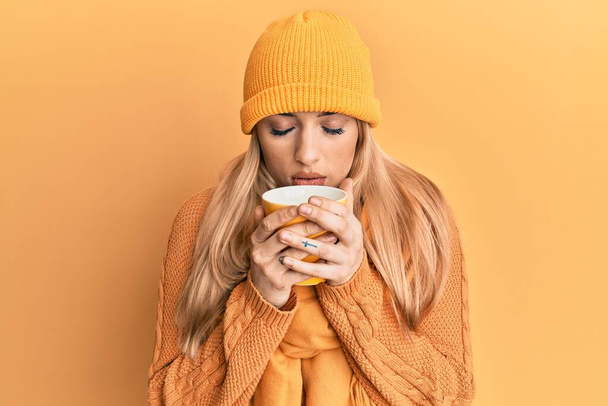 Young caucasian woman smelling coffee aroma over yellow background - Photo, Image