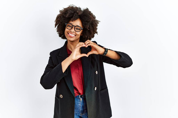 ビジネスジャケットと眼鏡を身に着けてアフロ髪を持つアフリカ系アメリカ人女性は手でハートシンボルの形をするのが大好きです。ロマンチックなコンセプト.  - 写真・画像