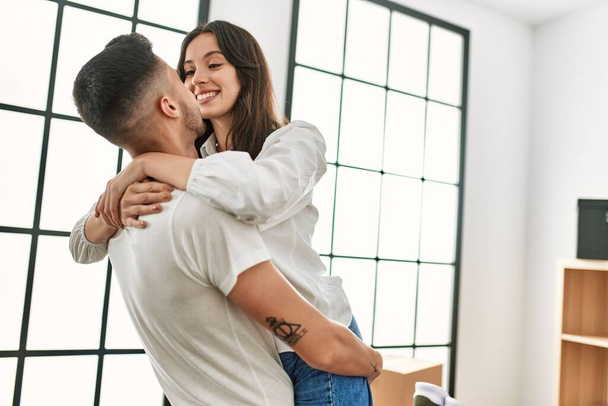 Joven hombre hispano sosteniendo a una mujer en brazos y abrazándose en un nuevo hogar. - Foto, Imagen