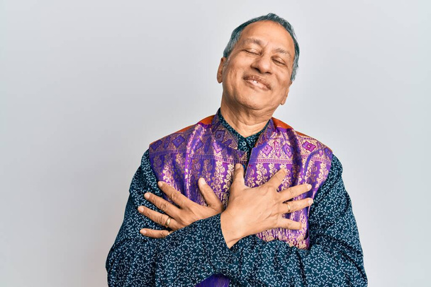 Keski-ikä intialainen mies yllään perinteinen intialainen vaatteita hymyillen kädet rinnassa, silmät kiinni kiitollinen ele kasvoilla. terveyskäsite.  - Valokuva, kuva