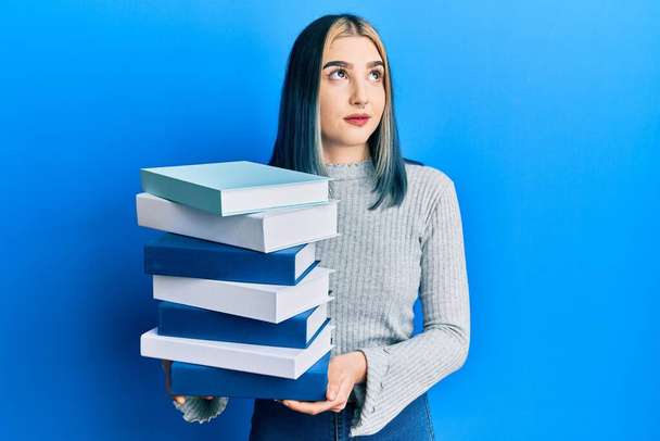Young modern girl holding a pile of books smiling looking to the side and staring away thinking.  - Foto, immagini
