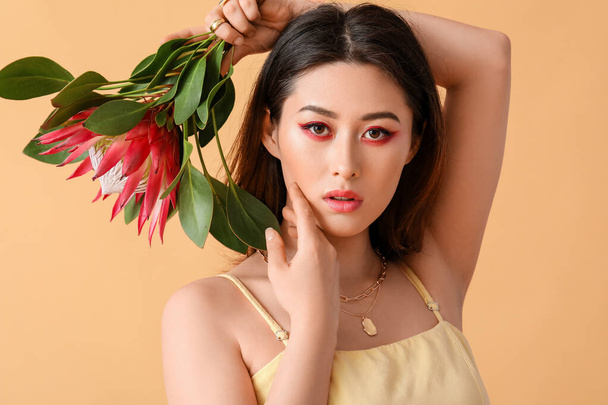 Mooie jonge vrouw met protea bloem op kleur achtergrond - Foto, afbeelding