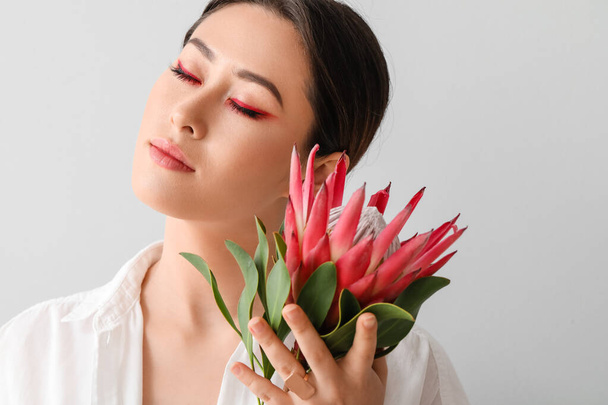 Beautiful young woman with protea flower on light background - Photo, Image