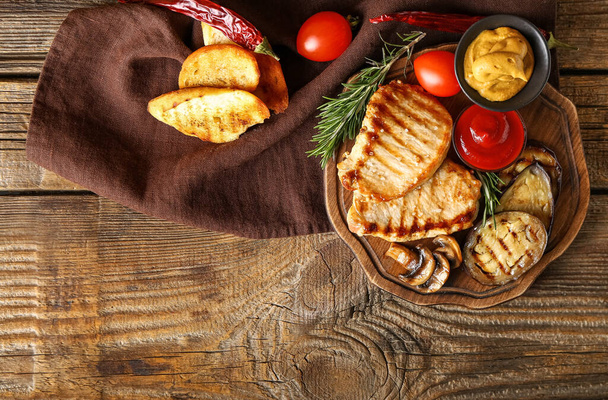 Доска с вкусными овощами и стейками на деревянном фоне - Фото, изображение