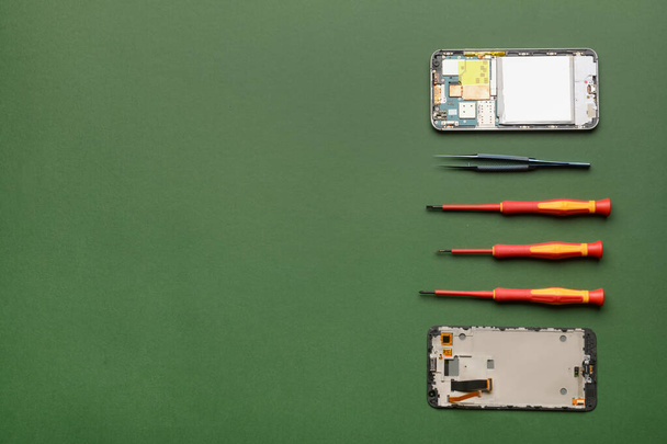 Gedemonteerde mobiele telefoon met technicus tools op kleur achtergrond - Foto, afbeelding