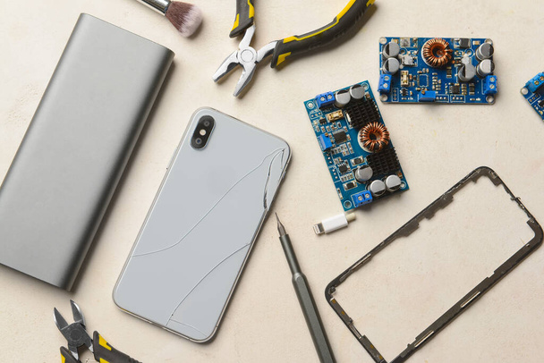 Beschadigde mobiele telefoon met technicus tools op lichte achtergrond - Foto, afbeelding