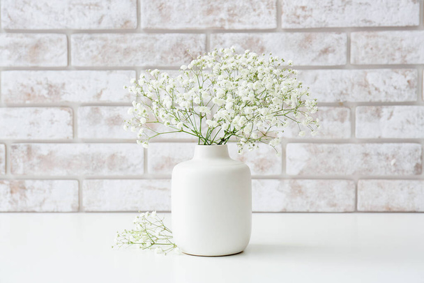 Vase with beautiful gypsophila flowers on table near light brick wall - Zdjęcie, obraz