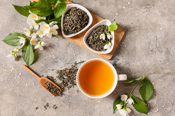 Bir fincan yasemin çayı, kuru yapraklar ve arkaplanda çiçekler ile kompozisyon - Fotoğraf, Görsel
